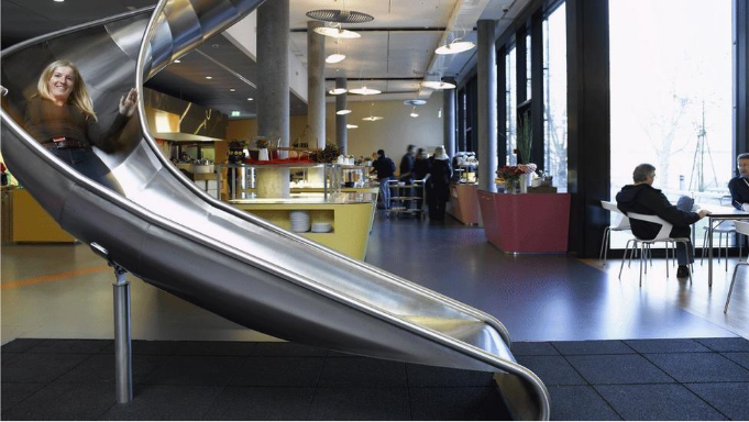 Woman sliding down a big silver slide inside a building.