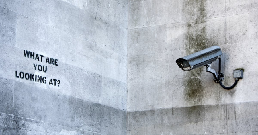Banksy art on wall with security camera and the words 'What are you looking at?'